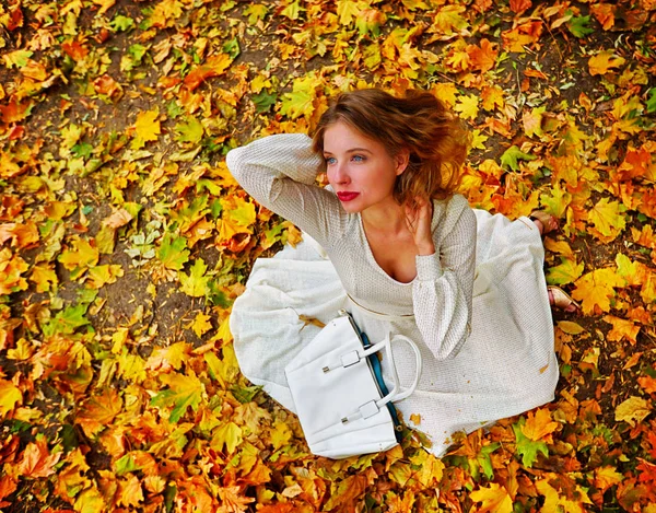 Осіннє модне плаття жінка сидить осіннє листя міського парку на відкритому повітрі . — стокове фото