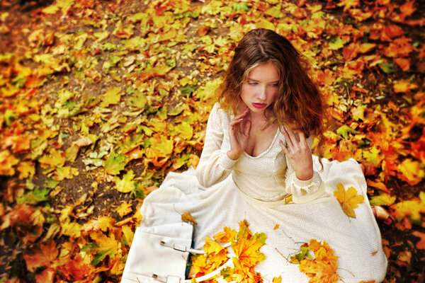 Autumn fashion dress woman sitting fall leaves city park outdoor.