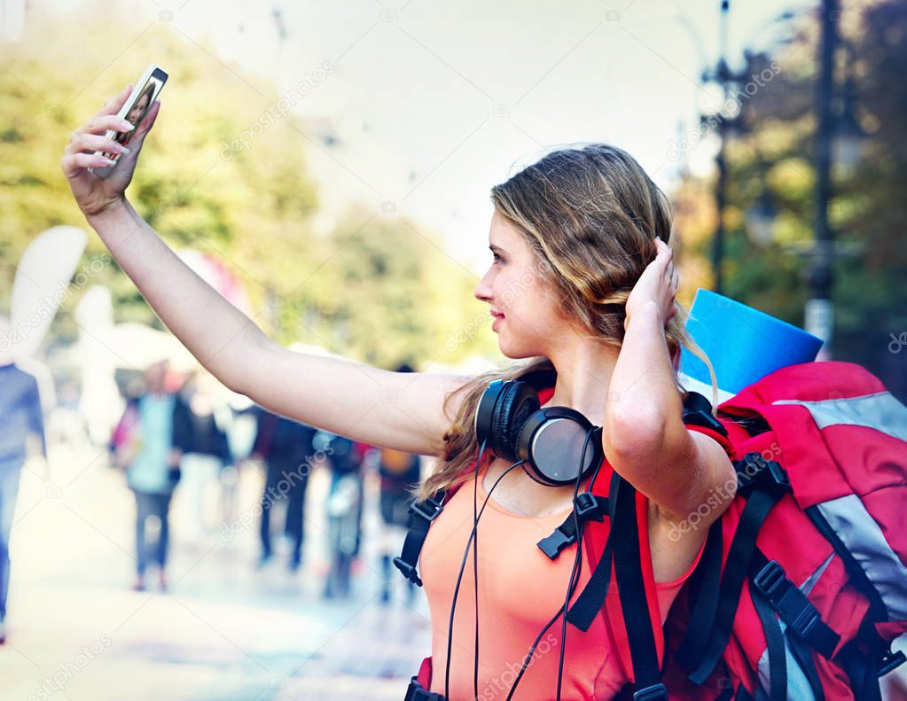 Tourist girl with backpack and headphones taking selfies on smartphone