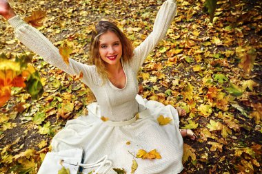 Autumn fashion dress woman sitting fall leaves city park outdoor. clipart