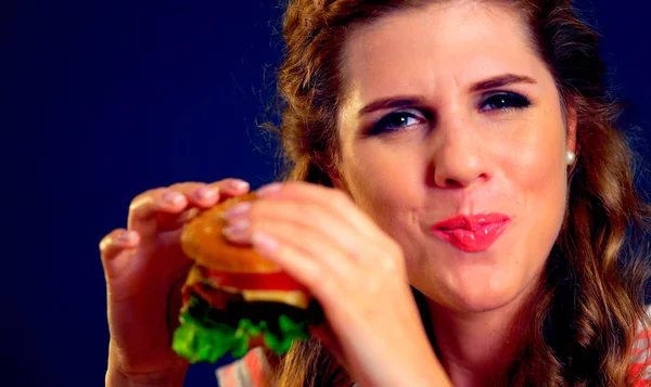 La mujer muerde hamburguesas y guiños. Feliz estudiante comer almuerzo sándwich . — Foto de Stock