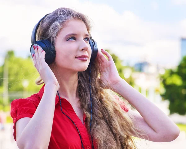 Chica en auriculares manos a la cabeza escucha música en la ciudad —  Fotos de Stock