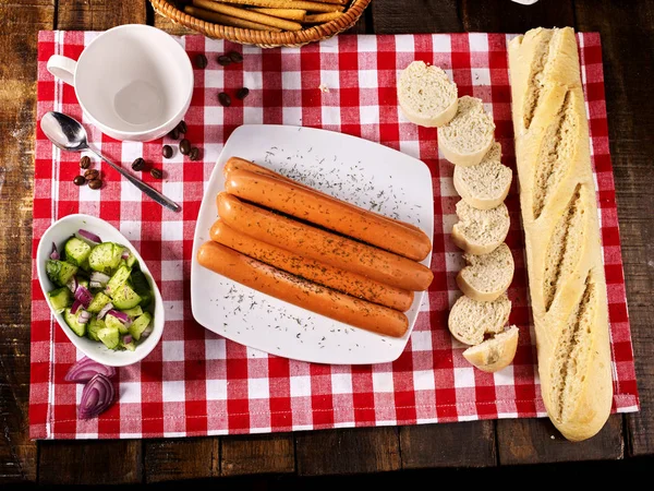 Porzione di salsiccia con baguette sulla tavola apparecchiata su un panno a quadretti — Foto Stock