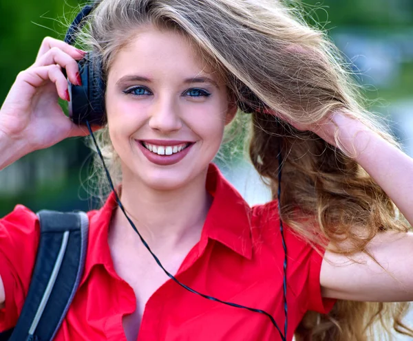 Estudante menina com mochila fone de ouvido ouvir música na grama verde — Fotografia de Stock