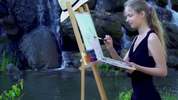 Girl draws on plein air mountain waterfall and lake background — Stock Video