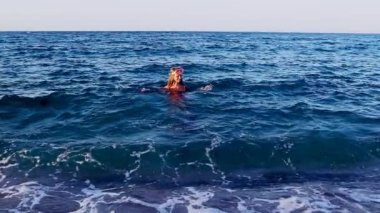 Kız kıyıdan uzakta deniz dalgalarında yüzüyor. Yavaş çekim