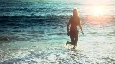 Yavaş hareket eden kadın deniz kumu boyunca suda koşuyor.