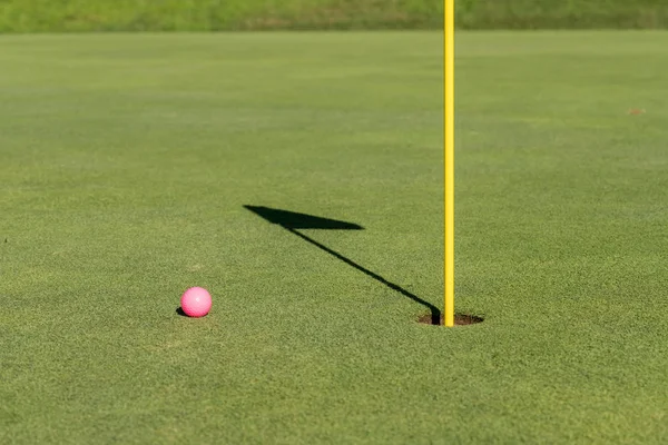 Pink golf ball by flag and hole on putting green — Stock Photo, Image