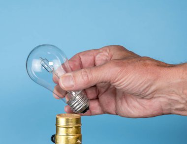 Senior man hand unscrewing the halogen bulb clipart