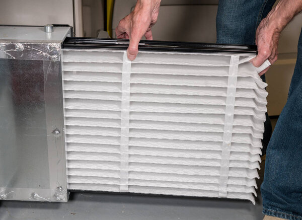 Senior man inserting a new air filter in a HVAC Furnace