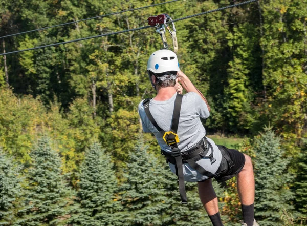 Rear view of a man on a zipline going down a valley in forest — Stock Photo, Image