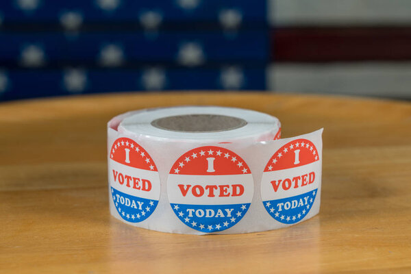 Roll of I Voted Today бумажные наклейки на столе с флагом США в фоновом режиме
