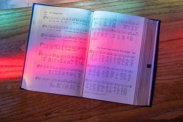Světlo z barevného skla okna dopadá na otevřené song knihu v americké církve — Stock fotografie