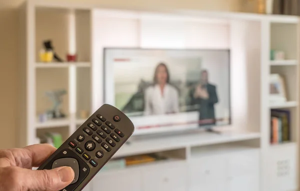 Mão masculina segurando controle remoto com TV no fundo — Fotografia de Stock