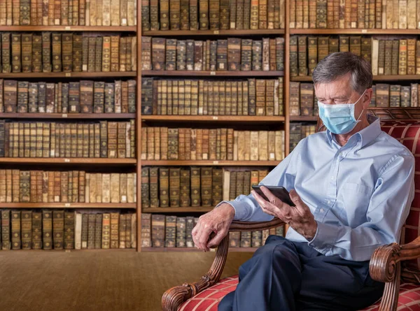Vanhempi mies kasvonaamio vastaan virus käsittelyssä eBook antiikkikirjastossa — kuvapankkivalokuva