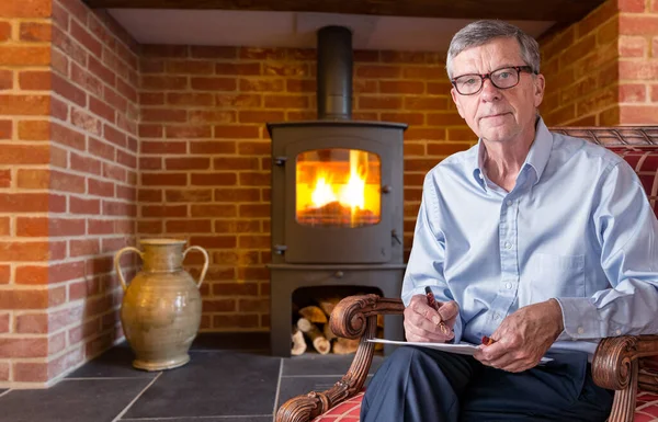 Senior homme avec lunettes vérifier un document avec cheminée en arrière-plan — Photo