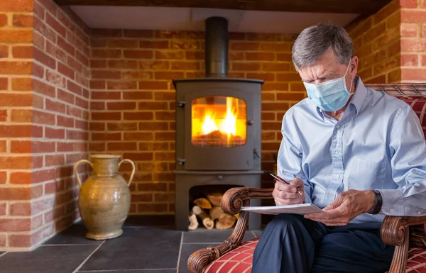 Bărbat în vârstă cu mască de față împotriva virusului verificarea unui document cu foc de lemn în fundal — Fotografie, imagine de stoc
