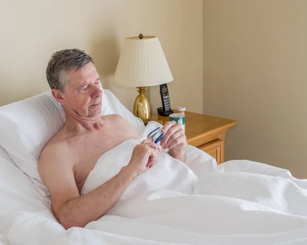 Svobodný kavkazský starší muž v nakloněné posteli kontroluje hladinu kyslíku v krvi — Stock fotografie