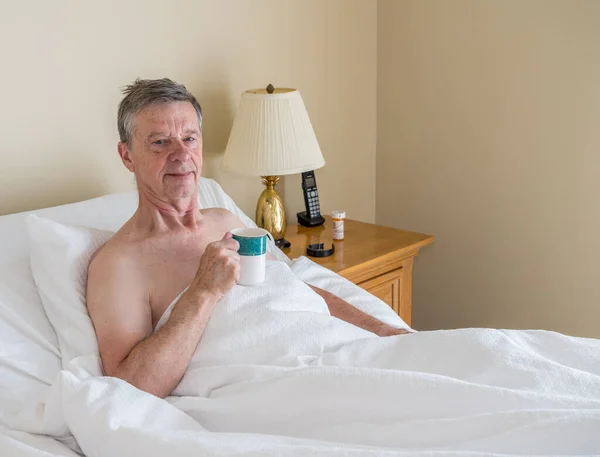 Hombre mayor caucásico soltero en cama inclinada y sonriendo hacia el espectador —  Fotos de Stock