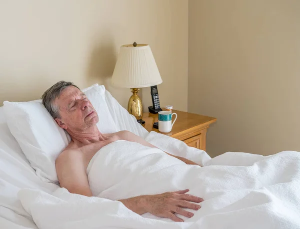 Single caucasian senior man in inclined bed and lying down asleep in light room — Stock Photo, Image