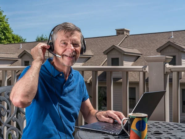 Senior man werkt vanuit huis op het buitenterras met headset en computer — Stockfoto