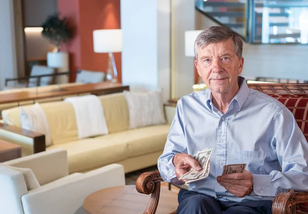 Idősebb férfi, aki kamerával szemben áll, és amerikai dollárt tart a kezében, mintha nézőnek adná át. — Stock Fotó