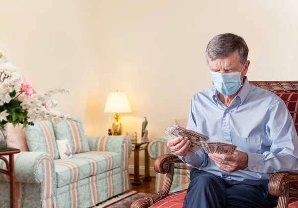 Senior man counting out US dollar bills with face mask and looking worried — Stock Photo, Image