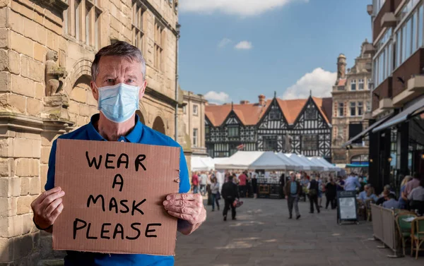 Bărbat în vârstă cu mască de față care deține un semn de carton cu poartă un mesaj de mască izolat împotriva albului — Fotografie, imagine de stoc