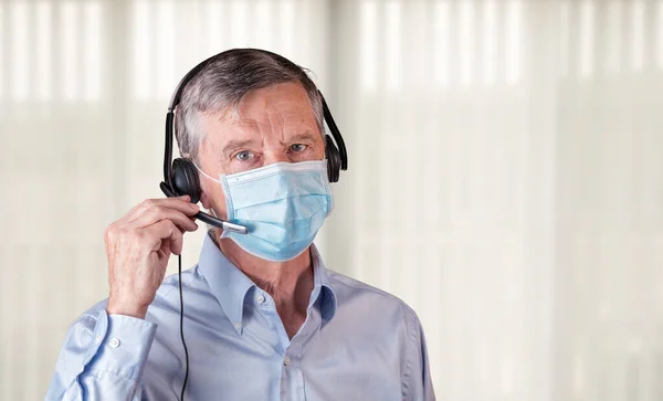 Ανώτερος άνθρωπος με μάσκα προσώπου χρησιμοποιώντας ακουστικά για να επικοινωνούν με την ομάδα ή τους πελάτες — Φωτογραφία Αρχείου