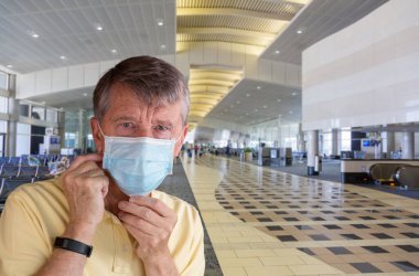 Yetişkin bir adam havaalanında maske takıyor ve çok endişeli görünüyor.