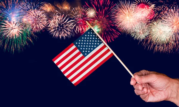 Mão de homem sênior segurando uma pequena bandeira dos EUA contra fundo fogos de artifício — Fotografia de Stock