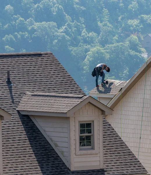 Young roofing contractor nailing shingles on a roof high above the ground — Stock Photo, Image