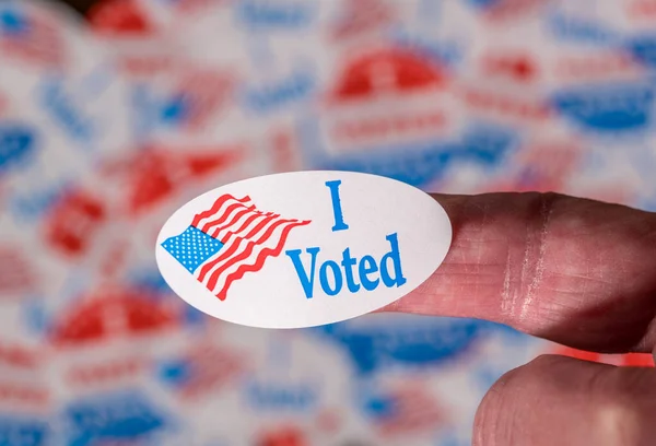 Finger with I Voted sticker in front of background created from many election voting badges — Stock Photo, Image