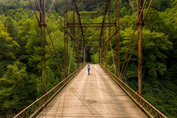チート川を渡ってジェンキンスバーグ橋を渡って犬を歩くシニア女性のドローンビュー — ストック写真