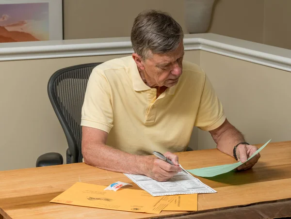 Högre kaukasisk man som sitter vid sitt skrivbord och fullföljer röstsedeln för frånvarande — Stockfoto