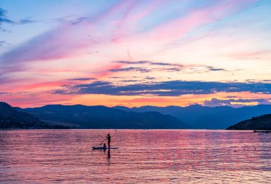 Dramatic sunset over Lake Chelan with silhouette of couple paddling on board and sky reflected in the smooth water of the lake in WA