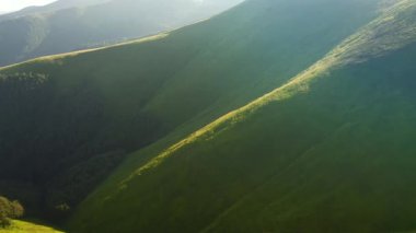 İnsansız hava aracı güneşin aydınlattığı yeşil dağ sıralarının üzerinden uçar. 4k 'lık bir videoda çekildi.