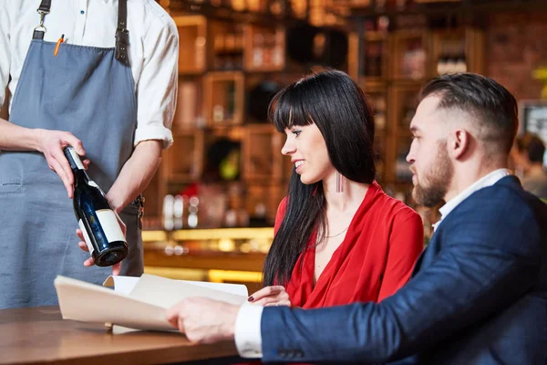 Servizio ristorante. giovane coppia e cameriere che offrono bottiglia di vino — Foto Stock