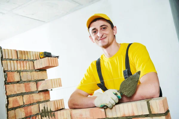 Metselaar. Portret van jonge lachende bouw mason in de buurt van bakstenen muur — Stockfoto