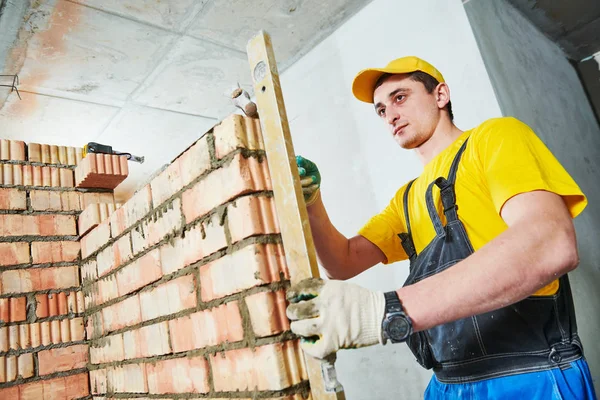 Colocação de tijolos. Verificações de trabalhadores erguido parede de tijolo com nível — Fotografia de Stock
