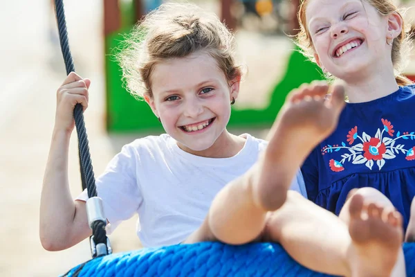 Amistad y diversión en la infancia. dos riendo joven chica en swing —  Fotos de Stock