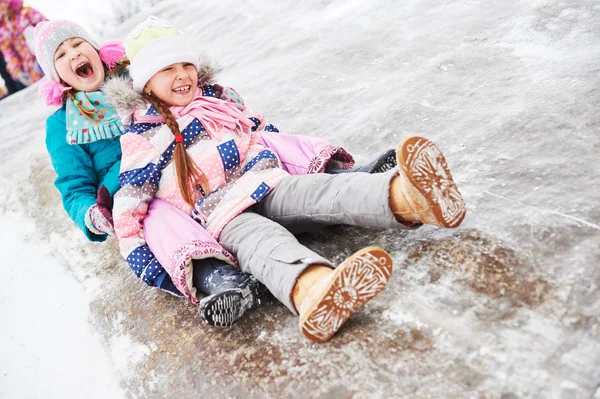 Дети веселятся катаясь на ледяной горке зимой — стоковое фото