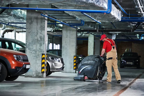 Werknemer met machine reinigingsvloer in parkeergarage. — Stockfoto