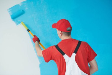 Painter worker with roller painting ceiling surface into white clipart