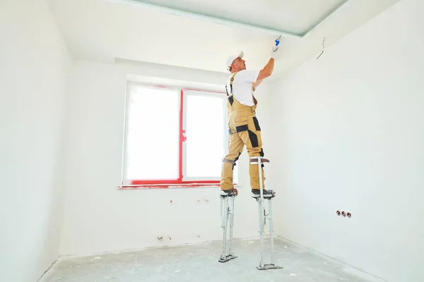 Painter in stilts with putty knife. Plasterer smoothing ceiling surface at home renewal — Stock Photo, Image