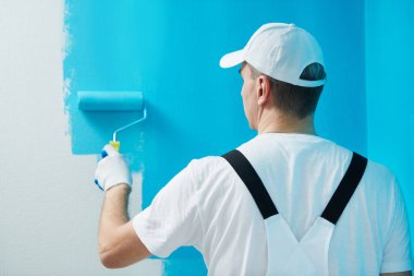Painter worker with roller painting wall surface into color clipart