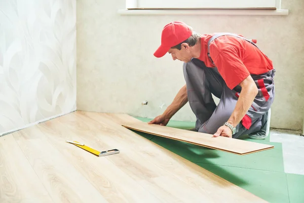 Работник кладет ламинат напольное покрытие при ремонте дома — стоковое фото