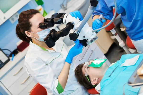 Dentist doing medical treatment male patient with microscope — Stock Photo, Image