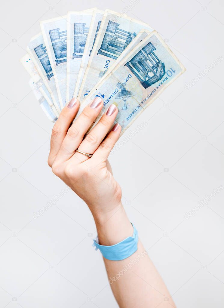 Female hand holding Tunisian paper money, ten dinares banknotes, a grey background