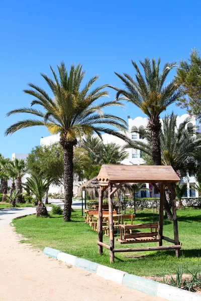 緑の芝生の上でピクニックや休憩のための木製のスイング テーブルや椅子を持つホテルのリゾートガーデン チュニジア — ストック写真